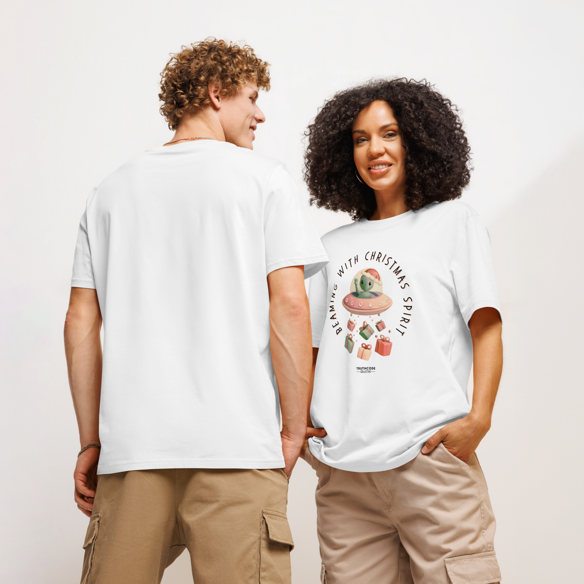Models wearing white organic t-shirt with cute alien in a spaceship Christmas-themed graphic and text 'Beaming with Christmas spirit'