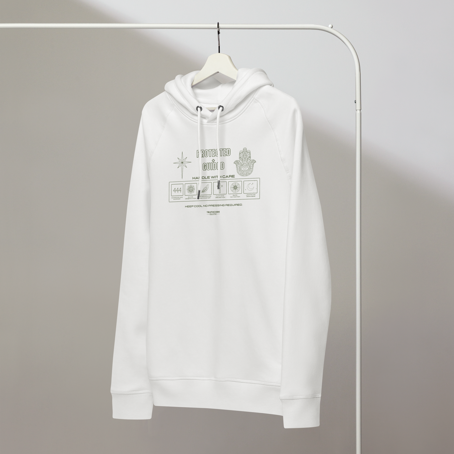 White organic hoodie with text 'Protected + Guided' with symbols and graphics related to it on a white hanger with a gray wall background