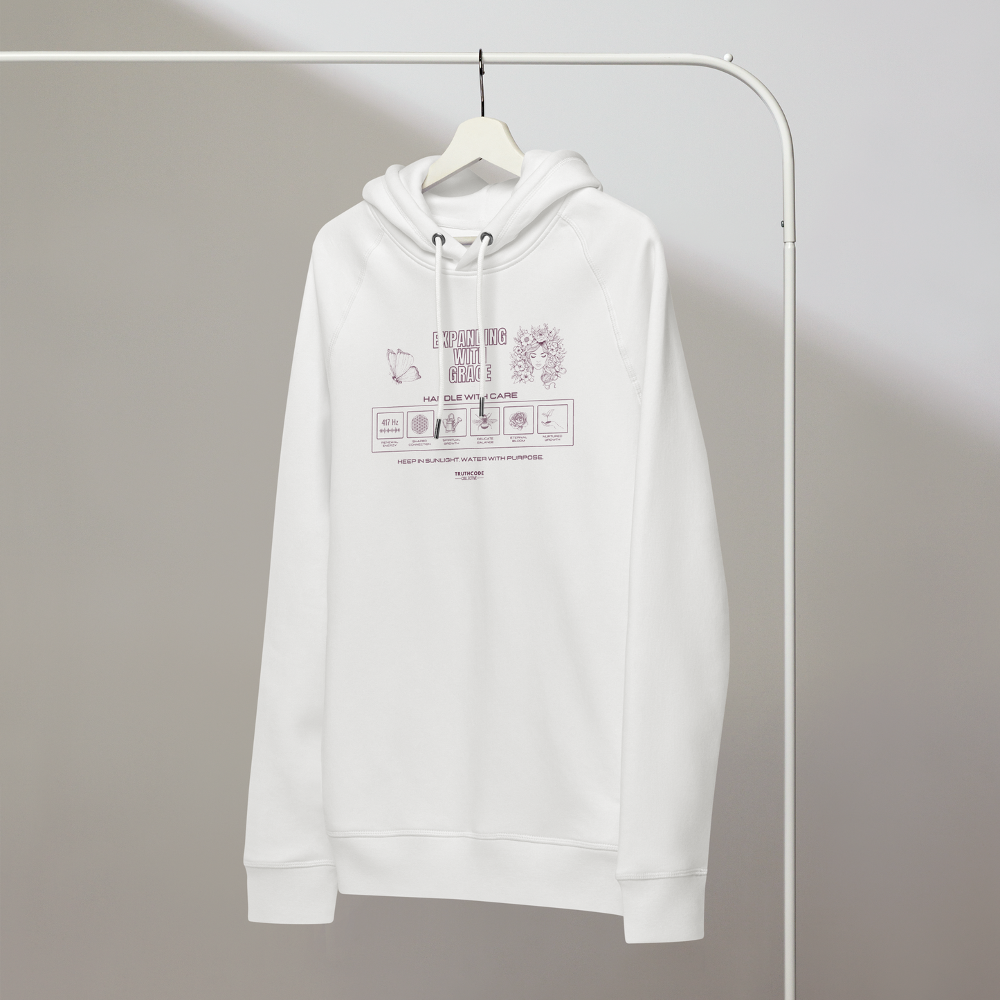 White organic hoodie with text 'Expanding with grace' with symbols and graphics relating to it on white hanger with a gray wall background