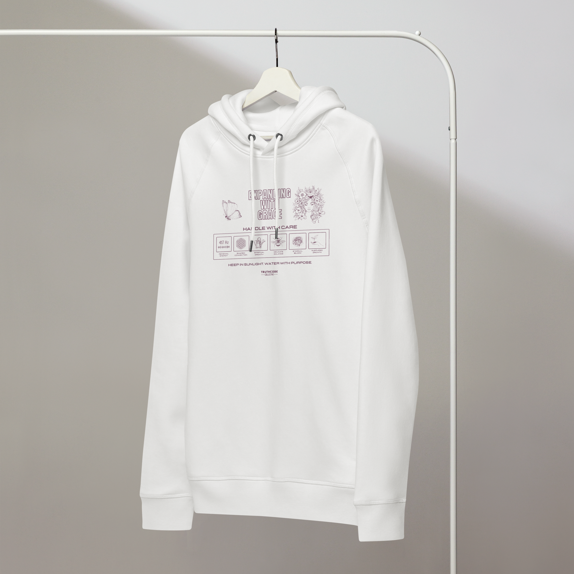 White organic hoodie with text 'Expanding with grace' with symbols and graphics relating to it on white hanger with a gray wall background