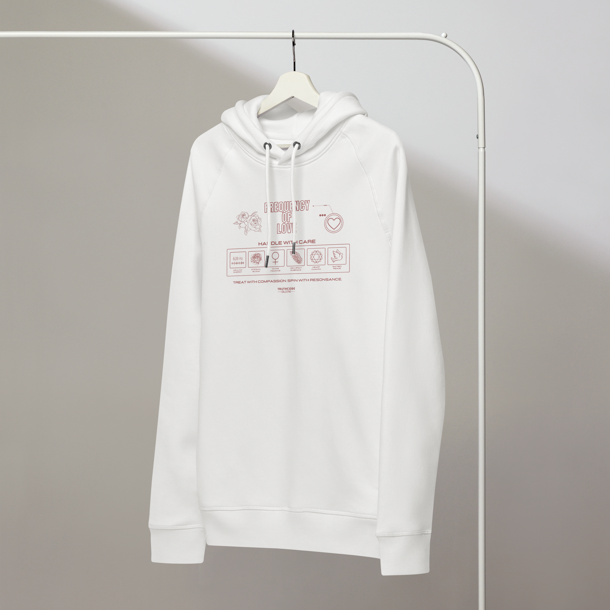 White organic hoodie with text 'Frequency of love' with symbols and graphics relating to it on a white hanger with a gray wall background